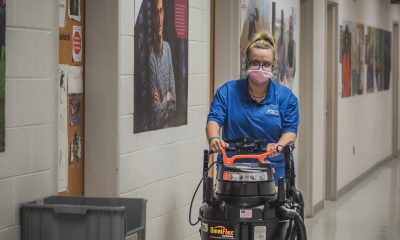 Housekeeper pushing a floor cleaner, while wearing a light pink mask.