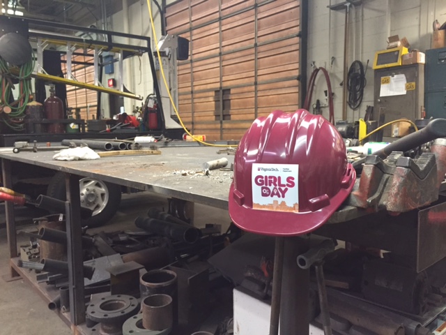 A Girls Day hard hat sitting on a table within a mechanical services shop.