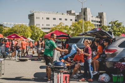 Office of Sustainability Graduate Assistant hands a recycling bag to a tailgater before a Virginia Tech football game while teaching them about recycling at Virginia Tech