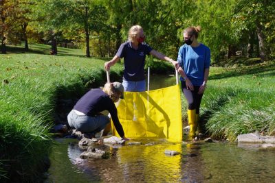 Three people standing in a creek with a yellow barrier