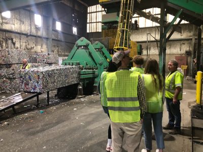 People in yellow safety vests touring recycling facility with large blocks of recycled items