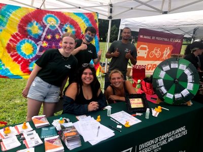 Office of Sustainability graduate assistants and student interns smile for a picture while tabling at Gobblerfest