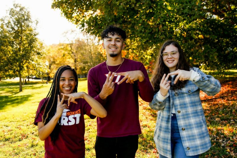 Three First Generation students enjoy a fall day on the Blacksburg campus as they show "VT" hand signs.