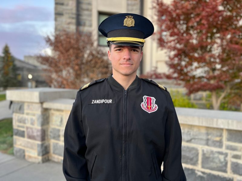 Cadet Zandipour stands in his uniform in front of a Hokie stone building, with changing leaves in the background.