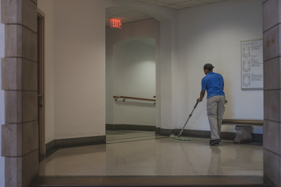 A housekeeper wearing a blue shirt sweeps the floor of Burruss Hall.