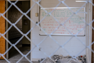 Randolph Hall mid-demo with a view through chain link construction fencing of a white board in a partially demolished room. There is still writing on the whiteboard, making an interesting juxtapositioning of the past and present.