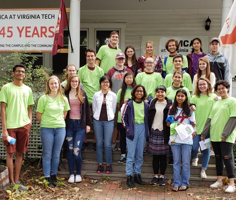 Green Game Day Tailgating team - a large group of people in green recycling shirts stand on the steps of the VT YMCA building.