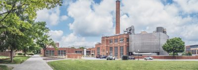 Central Steam Plant with cloudy blue skies behind it and green trees and grass surrounding it