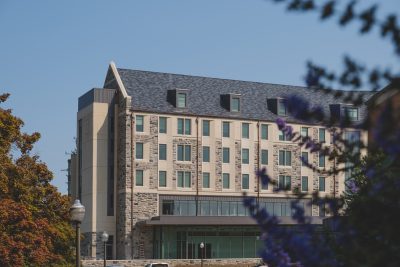 Photo of the CID residence hall with purple flowering branches in the foreground