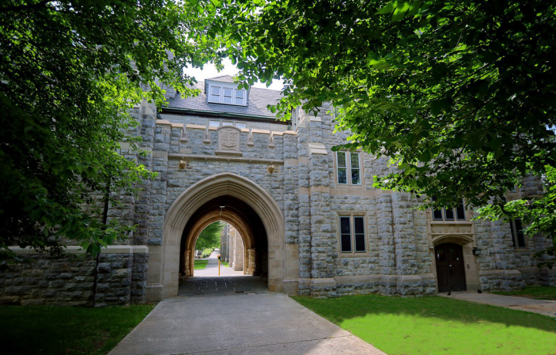 Tree leaves provide a frame around a photo of the arched breezeway tunnel surrounded by Hokie Stone at Eggleston Hall.