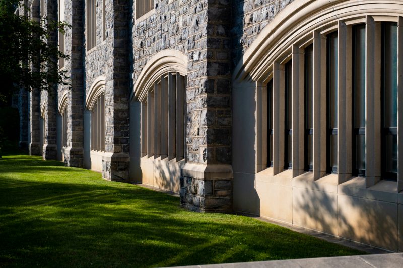 Sunlight and shadows from nearby trees accent arched windows surrounded by Hokie Stone on a campus building.