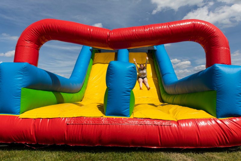 Giant, shiny and bright, multi-colored inflatable slide at Grad Bash with one happy student sliding down with her hands held high in the air.