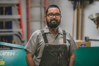 Portrait of James Pritchard wearing overalls and a grey button up shirt