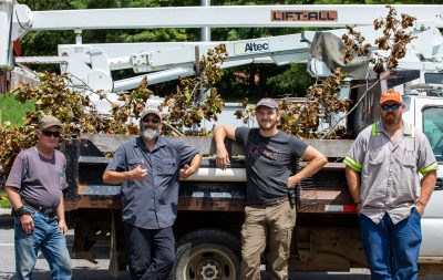 Four members of the urban forestry team stand in front of a bucket truck filled with tree branches. 