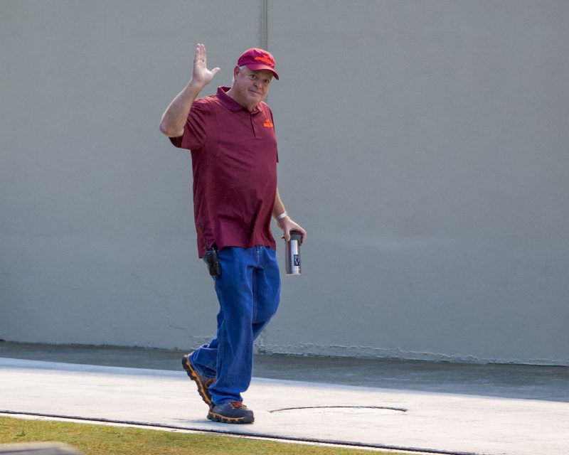 Jeff Trimble smiles and waves at the camera while walking inside of Lane Stadium