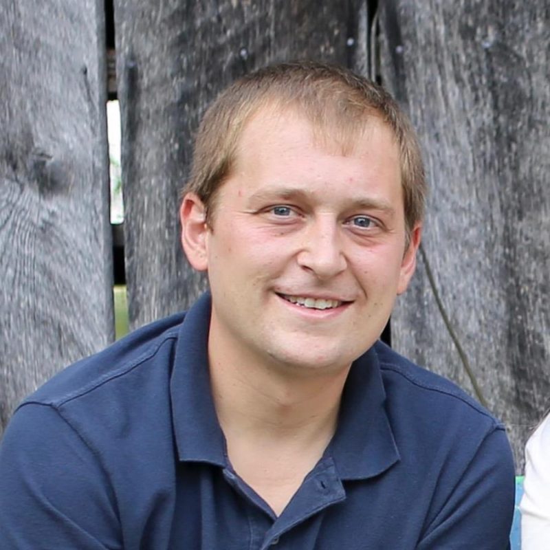 Casey Reece smiles at the camera while sitting against a wooden fence