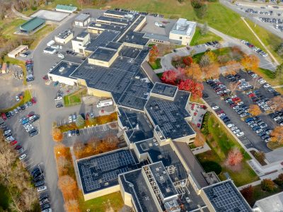 An aerial view of Virginia-Maryland College of Veterinary Medicine with solar arrays installed on the roof and fall colored trees surrounding the building.