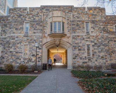 Grey Hokie Stone Norris Hall during a fall afternoon. A student walks in front of the building. 