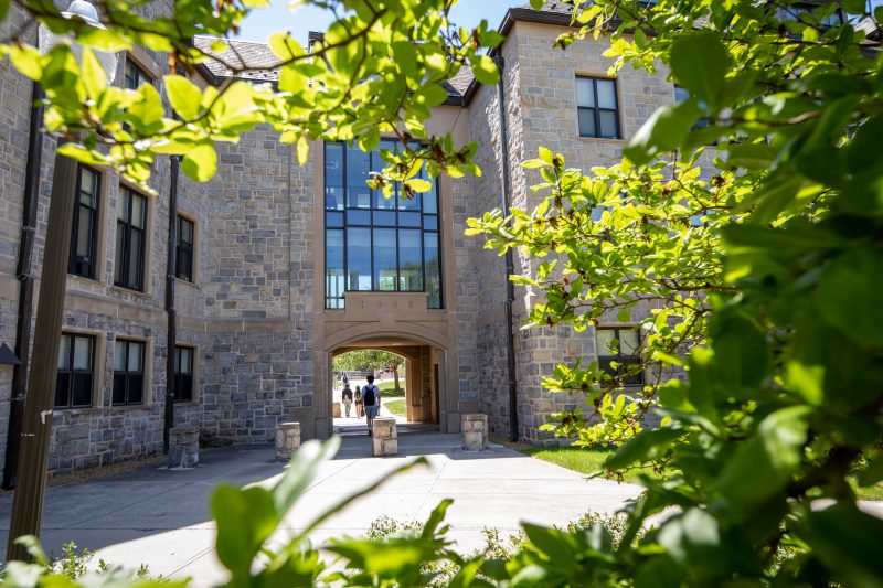 An exterior tunnel of a large grey Hokie Stone building with the view surrounded by green shrubbery