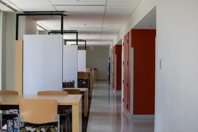 A hallway in a general classroom building. A series of wooden tables and patterned chairs spread across the hallway. 